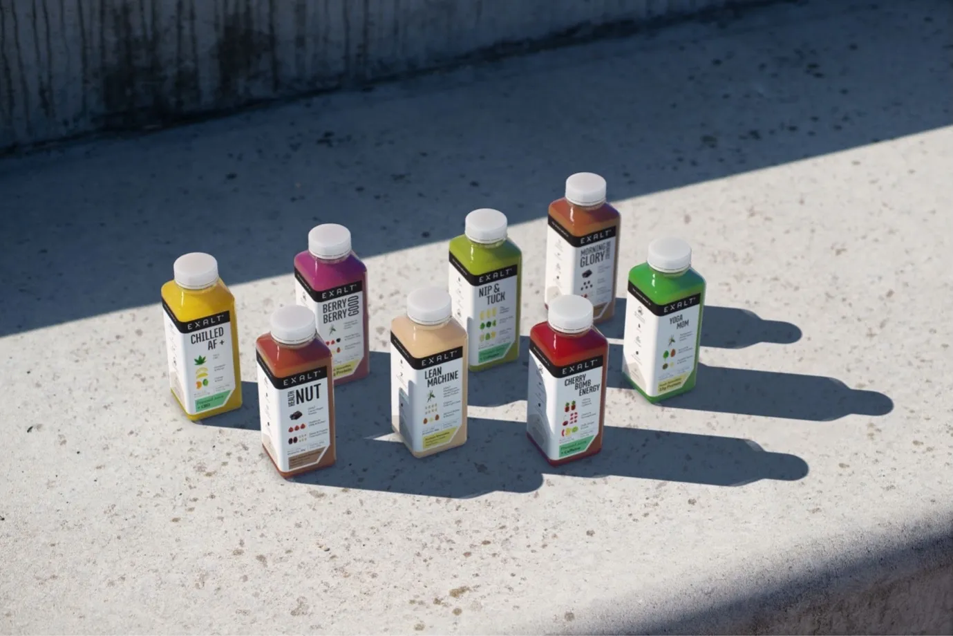 A range of EXALT cold-pressed drinks, set out in sunlight